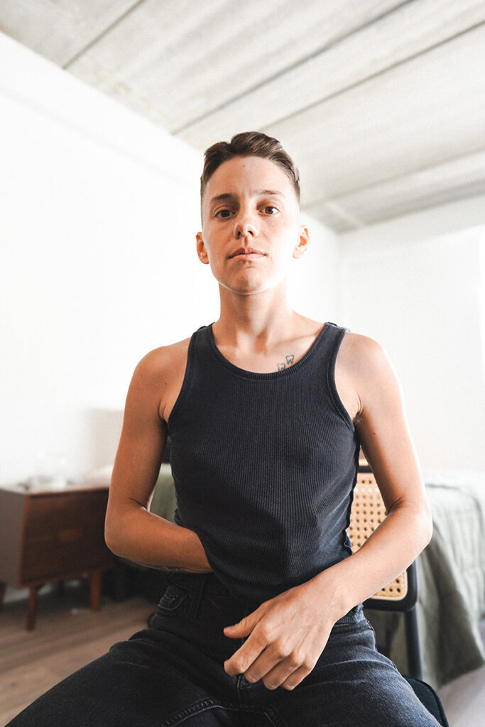 Ro White - Butch Lesbian in black tank top with strong arms out